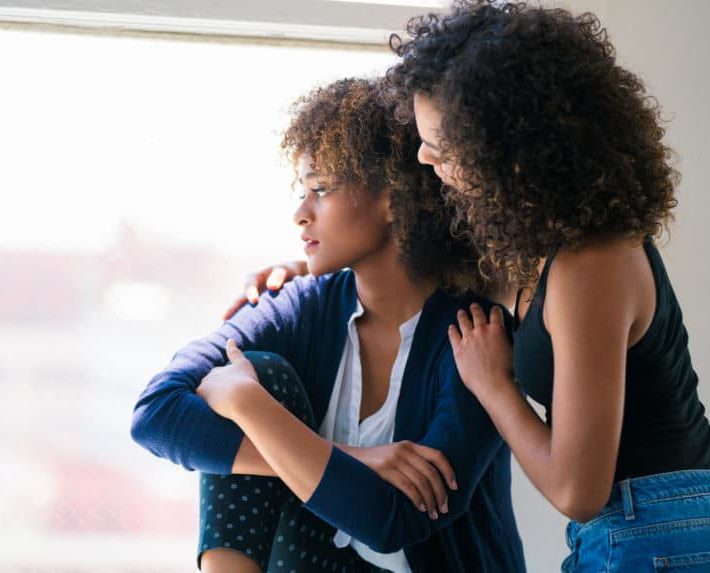 woman comforting another woman with her hands around her shoulders